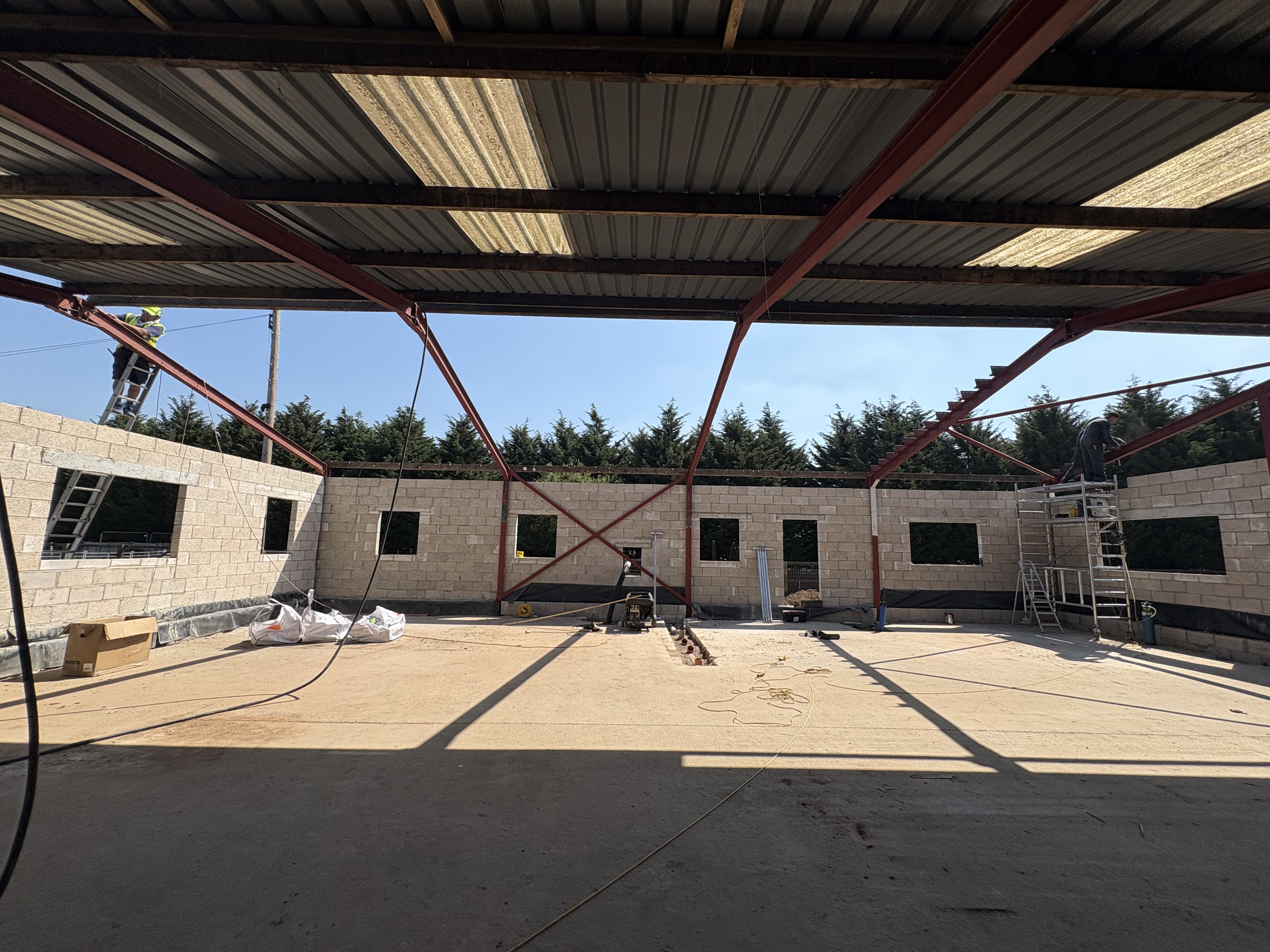 Interior of the barn during conversion — retained red steel portal frame with new insulated blockwork walls and window openings