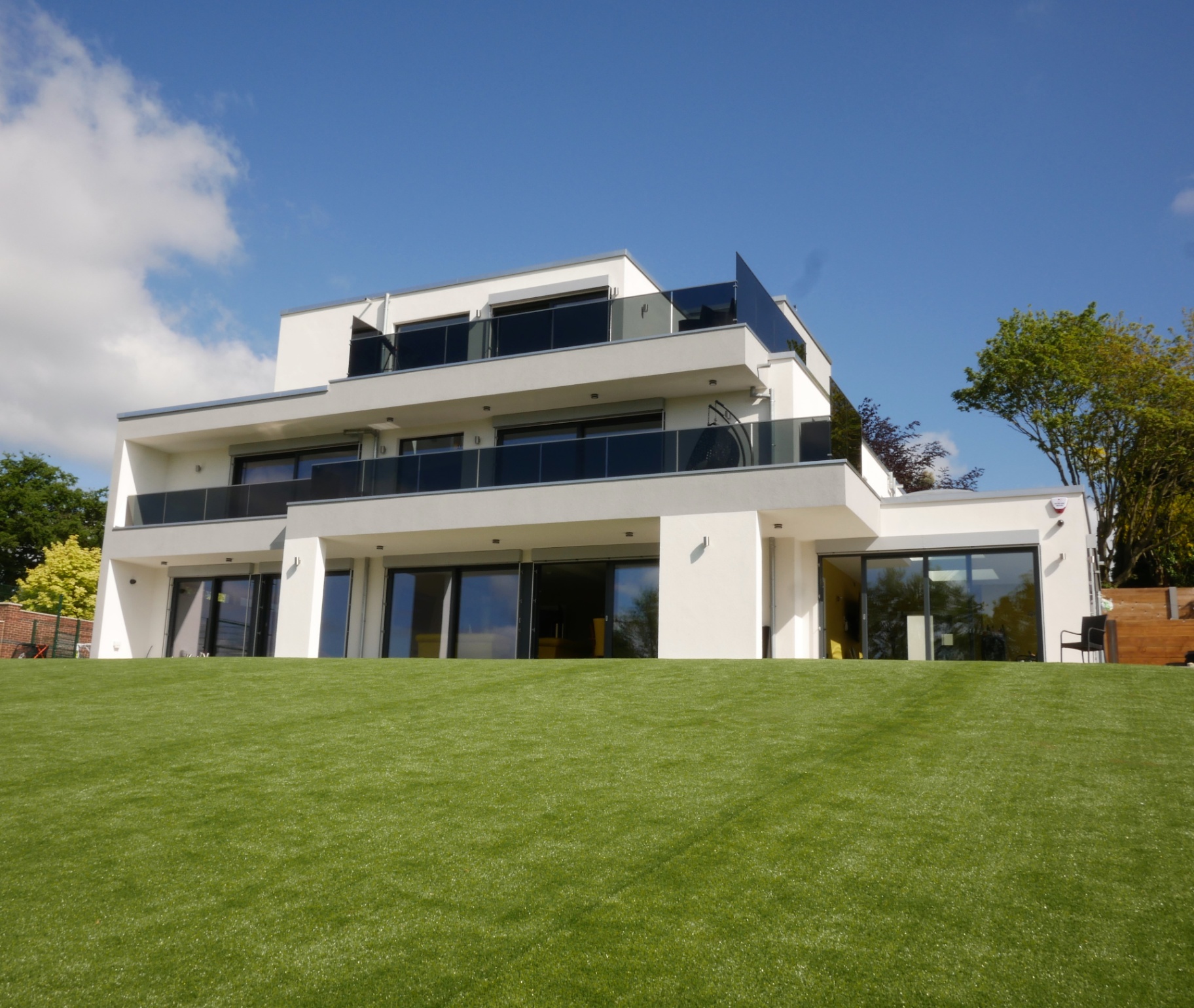 Three-storey contemporary white-rendered new build home with glass balconies and lawn