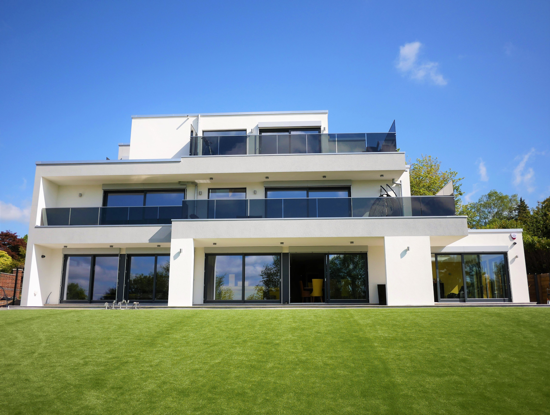 Rear elevation of the three-storey white-rendered contemporary new build with glass balconies overlooking the garden