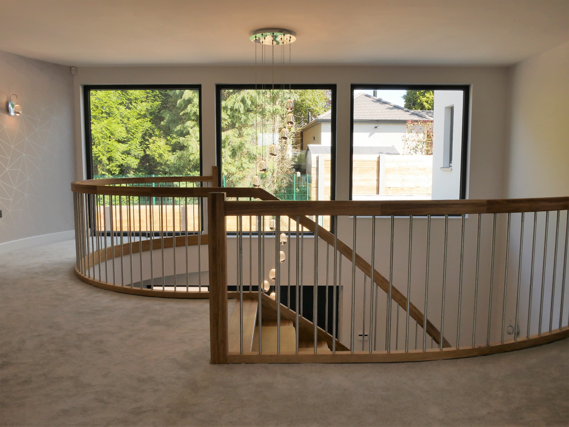 Bright first-floor landing with full-height picture windows framing the garden and curved oak balustrade