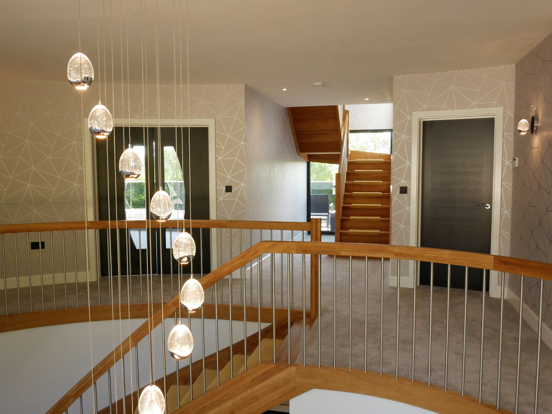 First-floor landing with cluster of glass pendant lights above a curved oak balustrade and oak feature staircase