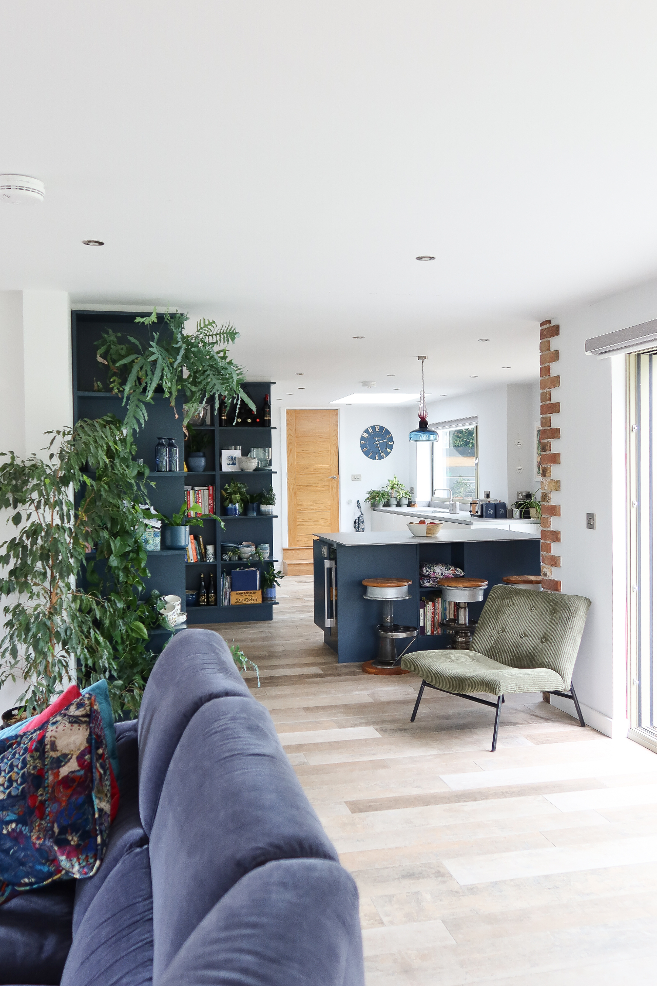 Open-plan living and kitchen space with navy joinery, exposed brick pier and countryside views