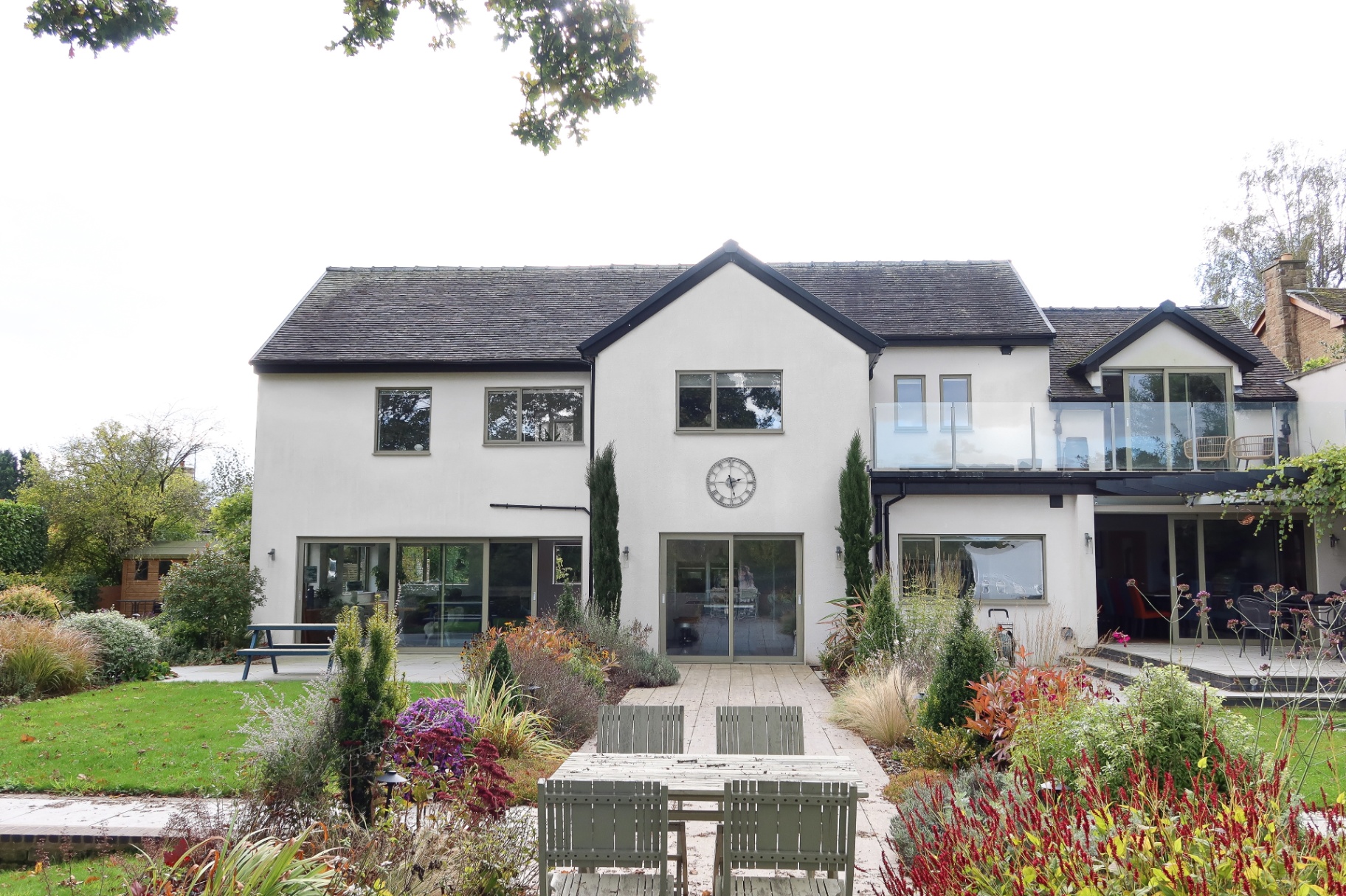Rear elevation of a remodelled family home with glazed balcony and mature garden